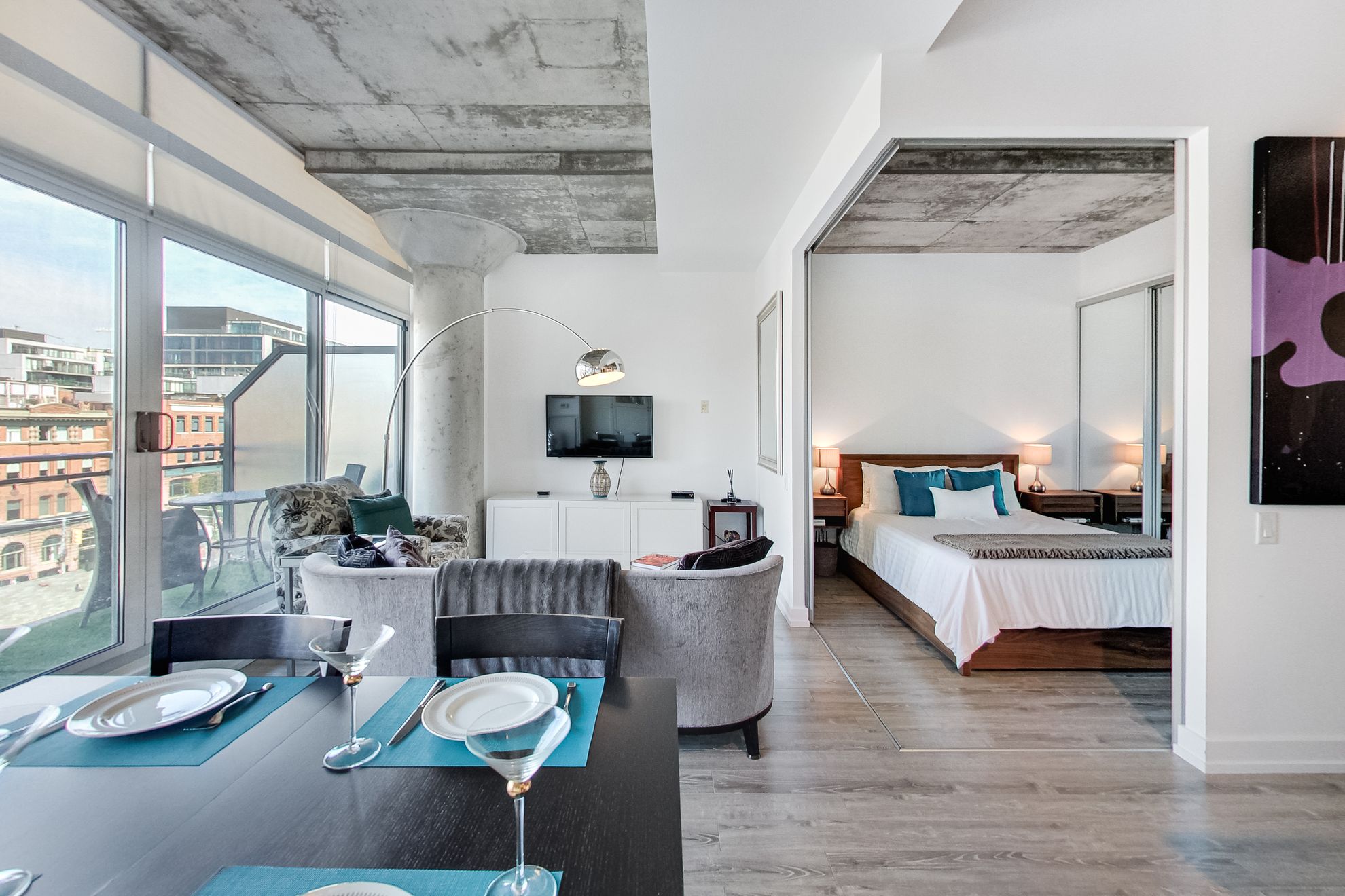 Modern open-concept loft condo with concrete ceiling, floor-to-ceiling windows, living and dining area, and bedroom